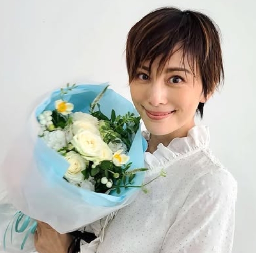 白い壁をバックに白い花束を顔に近づけて写っている米倉涼子さん