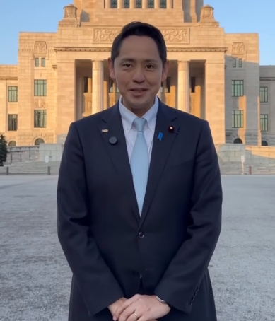 深作ヘススさんが国会議事堂をバックにスーツ姿で立つ写真