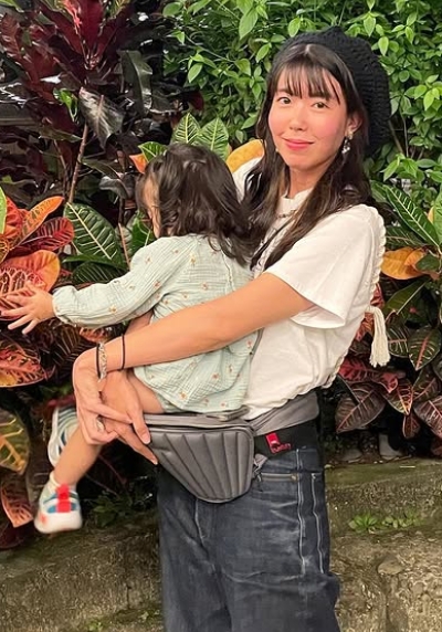 植物をバックにわが子を立った状態で抱きかかえている石橋穂乃香
