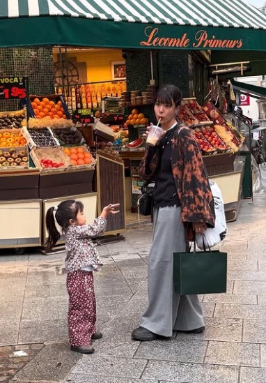 フランスのパリの街頭の果物屋の前で娘と飲み物を飲みながら散歩している石橋穂乃香さん