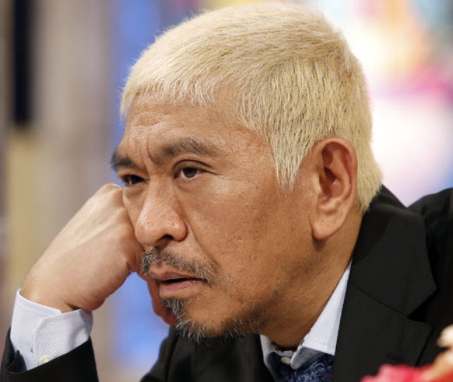 スーツ姿で右手で頬杖をついている松本人志