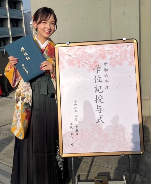 日本大学芸術学部演劇学科の学位授与式と書いたプレートの横に立つはかま姿の光嶌なづな