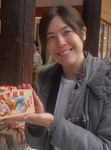 吉備津神社で絵馬を手に取っているグレーのフードのあるコートを着ている小野田紀美