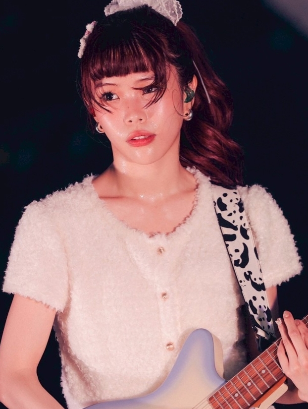 ライブステージでギターを演奏するアイナ・ジ・エンド。白いトップスとレースのヘッドバンドを着用し、牛柄ストラップのギターを持ちながら熱唱している姿