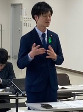 会議室で勉強会に参加して起立して意見を述べている鈴木憲和