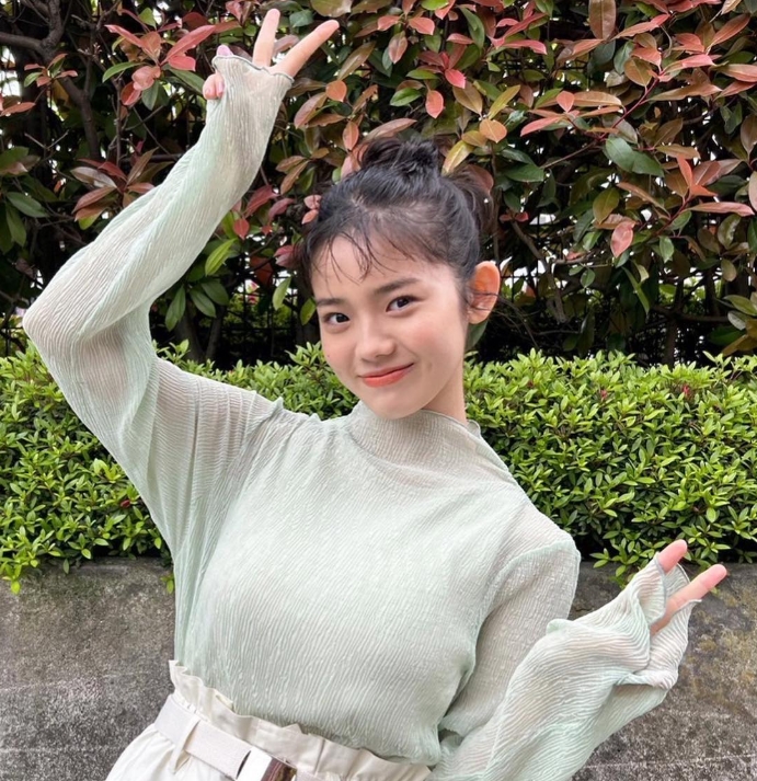 淡いライトグリーンの長袖トップスに白いベルト付きスカートを合わせたナチュラルなコーデ姿の志田こはく