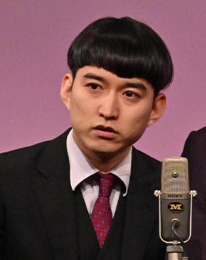 黒のスーツで漫才中のめぞんの吉野おいなり君