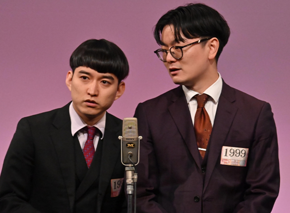 お笑いコンビ「めぞん」の2人がスタンドマイクを前にして漫才をしている画像