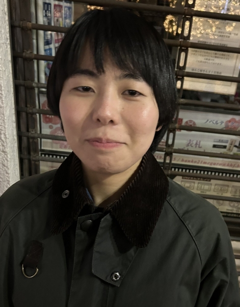 ヨネダ2000の誠さんが夜の書店前で緑のジャケットを着て立っている様子