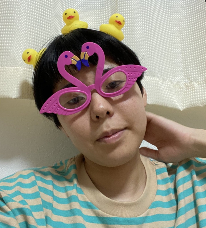 お笑いコンビ・ヨネダ2000の誠がピンクのアヒルのサングラスとひよこのヘッドバンドを着用したユニークな姿