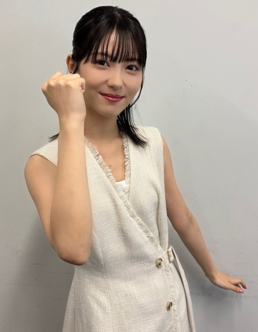 浜辺美波がノースリーブのワンピース姿で、拳を握ってポーズをとる姿。前髪ありのストレートヘアで、壁の前に立ち、力強い表情を見せている。