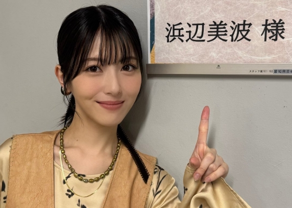 浜辺美波が控室の前で、自身の名前が書かれた案内札を指差している様子。前髪ありの黒髪ストレートヘアで、ベージュとブラウンの衣装に緑のネックレスを着用。